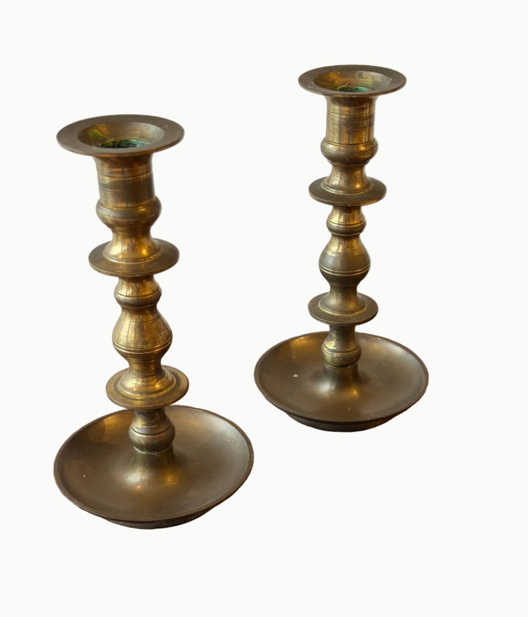 Pair of brass candlesticks on a wooden surface with a white background