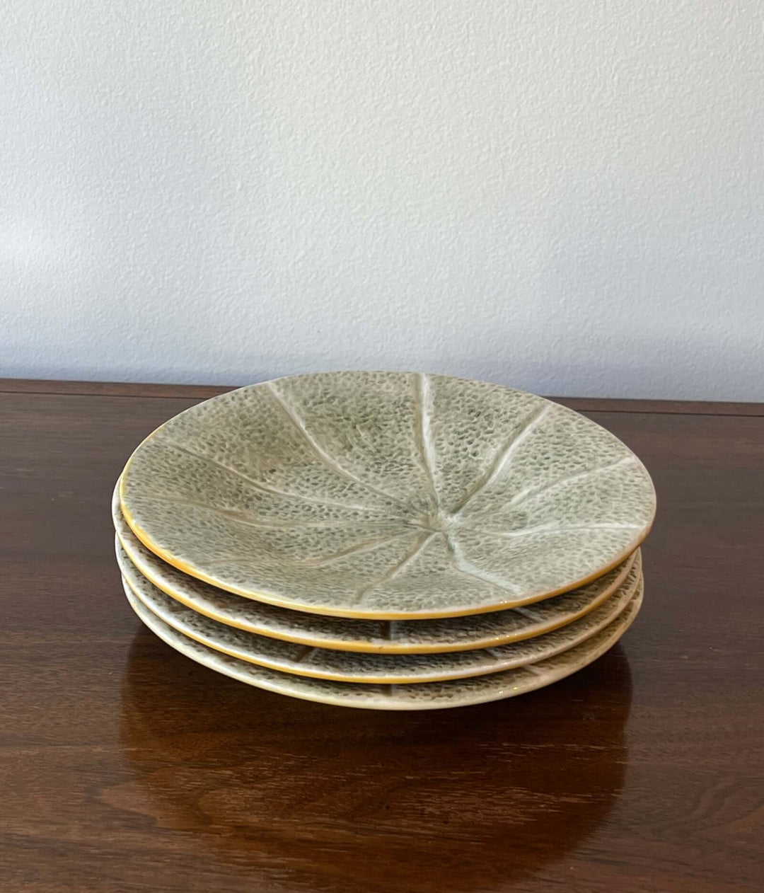 Set of Bordallo Pinheiro Melon Dessert Plates from Portugal stacked on a wooden table with a soft celadon-green glaze.