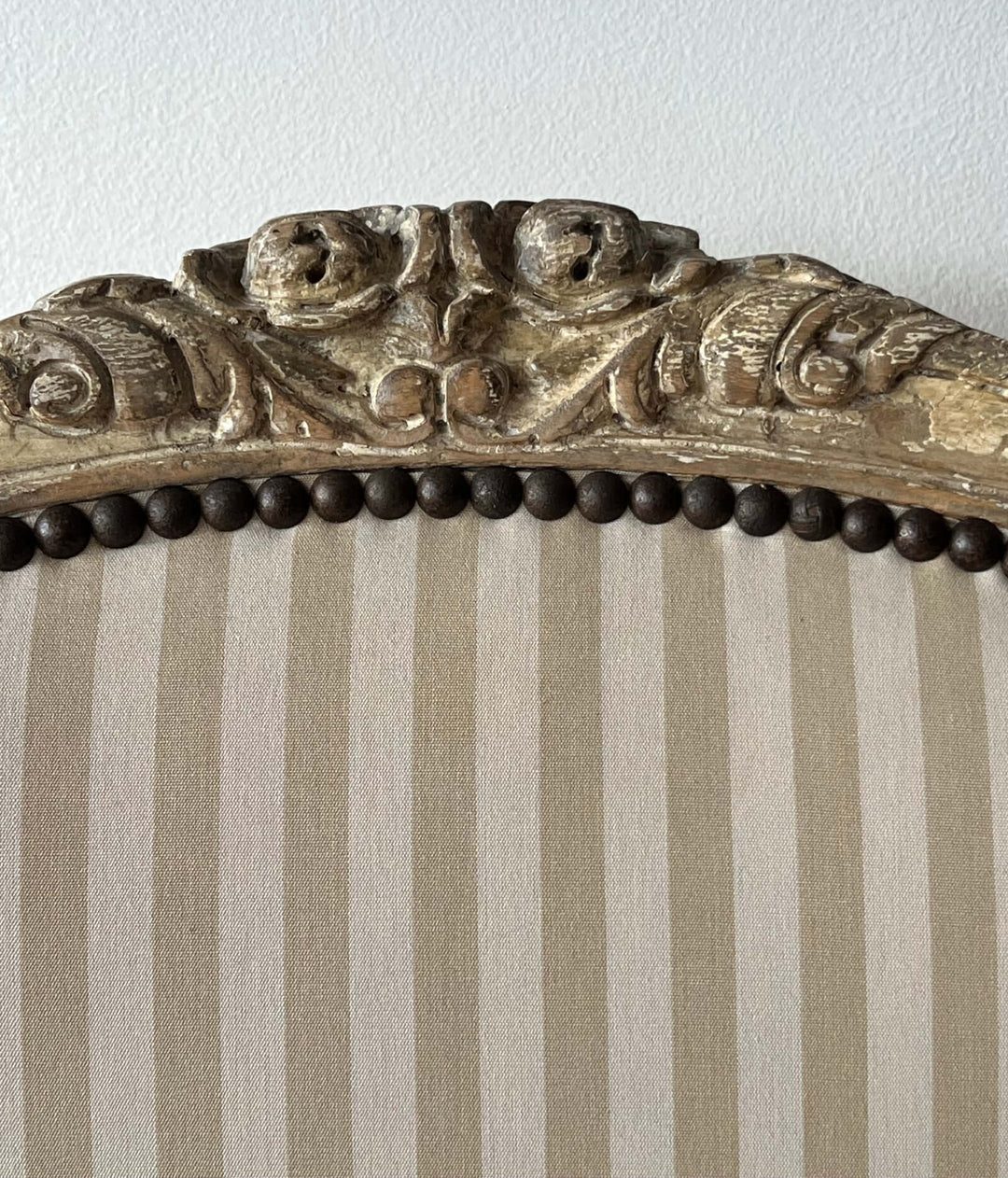 Detail of the carved crest and striped upholstery of a Pair of Vintage Louis XV Style Fateuil armchair.