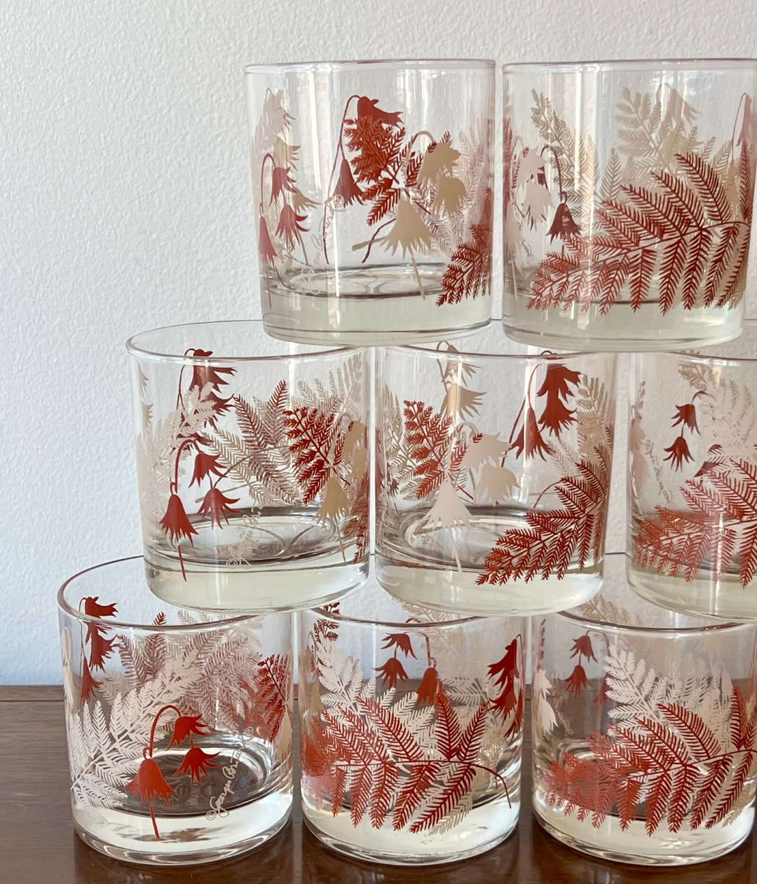 Stack of glass tumblers with floral designs on a plain background
