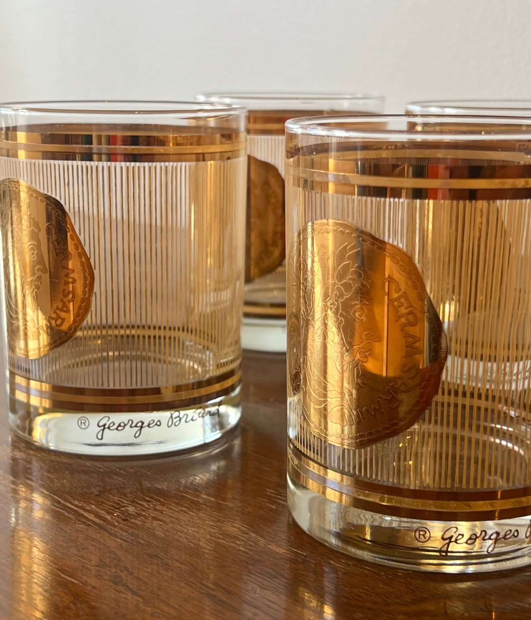 Set of three glass tumblers with gold accents and engraved designs on a wooden surface.