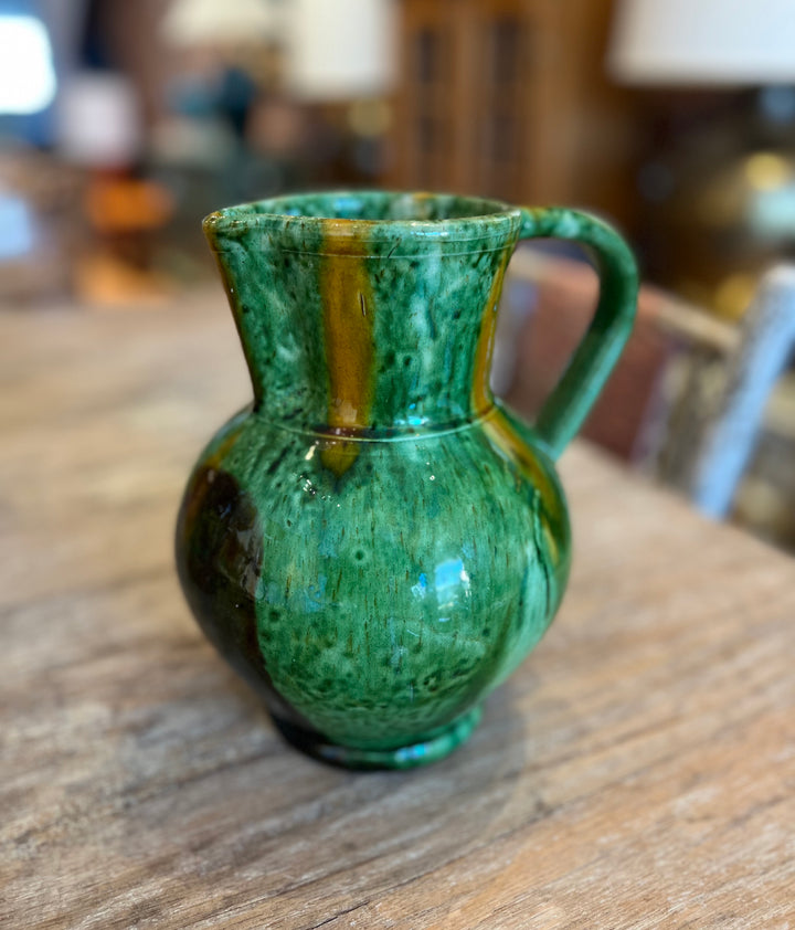 Green ceramic pitcher on a wooden surface with a blurred background