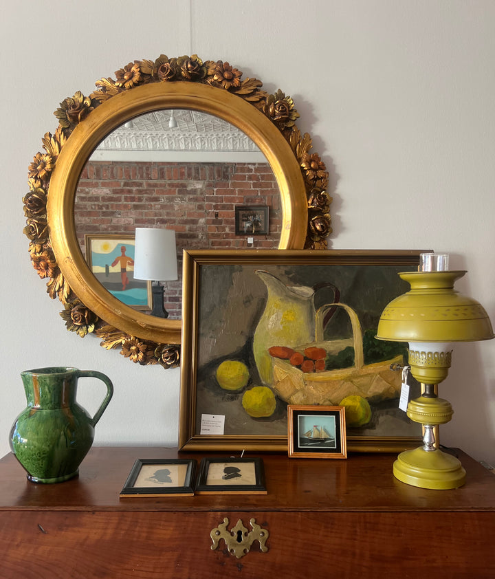Decorative items including a gold-framed mirror, green pitcher, painting, and yellow lamp on a wooden surface.