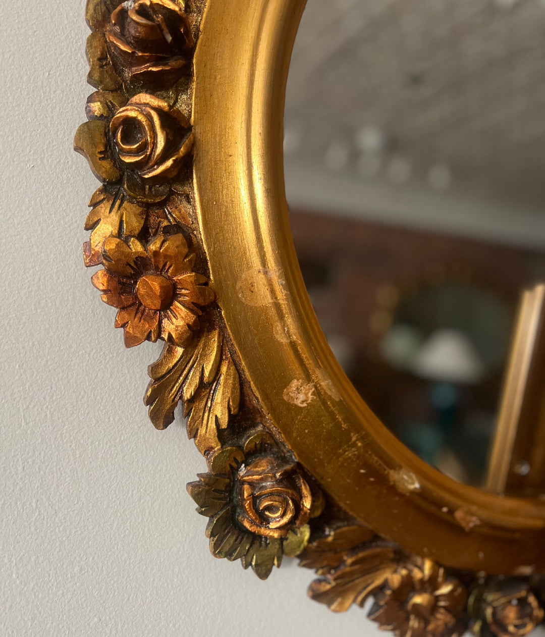 Decorative gold mirror with floral detailing on a plain wall.