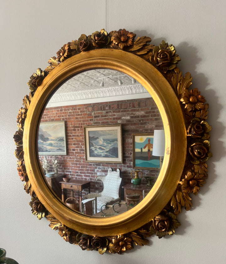 Decorative gold-framed mirror on a wall with a reflection of a room.